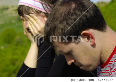Photo of a young couple unhappy sad negative disagreements, conflicts, morose, bad problems, bored, sitting on a field in the mountains  87334922