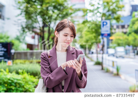 Smiling business woman operating a smartphone 87335497