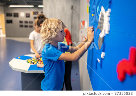 Profile of boy attaching lego piece to wall Profile of boy attaching lego piece to wall 87335828