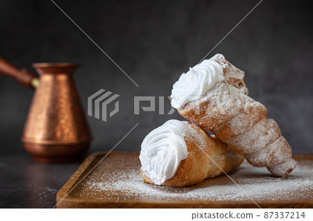 Puff pastry horns filled with white cream and powdered sugar Puff pastry horns filled with white cream and powdered sugar 87337214