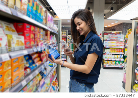 Close up of asian woman is shopping for product and scanning barcode with smartphone at supermarket. 87338447