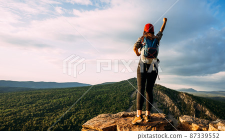 A traveler with a backpack in the mountains at sunset. A traveler with a backpack on the background of mountains, rear view. Hiking trips. A tourist girl on the background of a mountain landscape 87339552