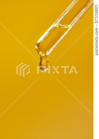 A drop of cosmetic aromatic oil drips from the pipette. Front view. A drop of cosmetic aromatic oil drips from the pipette. Front view. 87339805