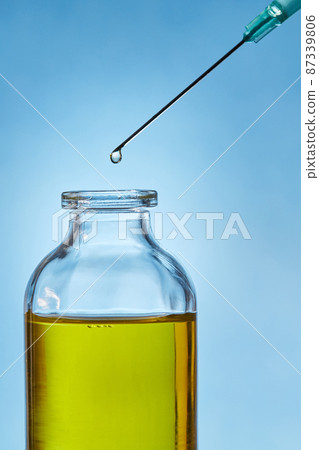 A drop of liquid drips from the needle of a medical syringe into the bottle. Front view. Macro photo. A drop of liquid drips from the needle of a medical syringe into the bottle. Front view. Macro photo. 87339806