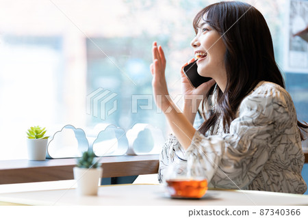 一位年輕女子向正在咖啡館見面的朋友揮手致意 87340366