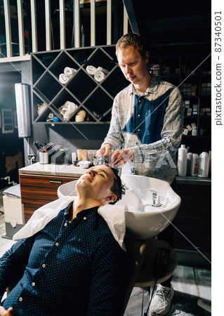 a brunet man washes hair with a hairdresser in a barbershop.  87340501