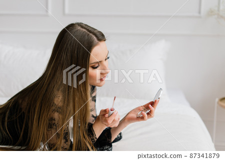 Beautiful lady doing her make up and hair in bedroom. Attractive young female with pretty long hair 87341879