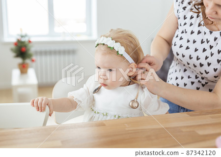 Mother helps to put on cochlear implant for her deaf little daughter. Hearing aid and deafness concept Mother helps to put on cochlear implant for her deaf little daughter. Hearing aid and deafness concept 87342120