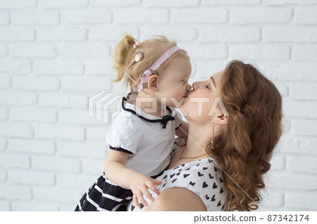 Mother holds her child with hearing aids and cochlear implants on white brick wall . Deaf and health concept 87342174