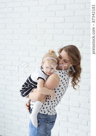 Mother holds her child with hearing aids and cochlear implants on white brick wall . Deaf and health concept 87342181