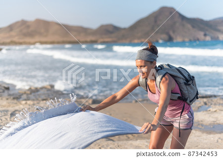 Female traveler spreading towel on sandy seashore Female traveler spreading towel on sandy seashore 87342453