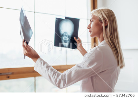 Female radiologist looks at scans of skull. Female radiologist looks at scans of skull. 87342706
