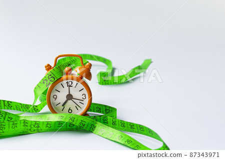 measure tap with orange clock on white wooden background. Diet concept. measure tap with orange clock on white wooden background. Diet concept. 87343971