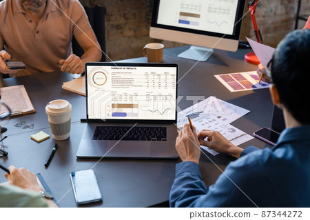 Close-up of business people sitting at the table with laptop and looking at monitor with financial grpahs during teamwork at meeting 87344272