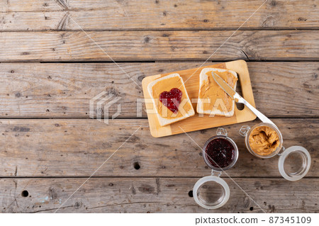 Overhead view of open face peanut butter and jelly sandwich on serving board with jars at table 87345109
