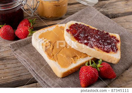 Close-up open face peanut butter and jelly sandwich on napkin with jars and strawberries at table Close-up open face peanut butter and jelly sandwich on napkin with jars and strawberries at table 87345111