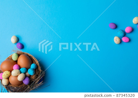 Easter eggs with colorful candies in nest on blue background with copy space 87345320