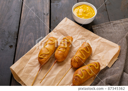 Close-up of mustered sauce on corn dogs over paper bag at wooden table 87345362