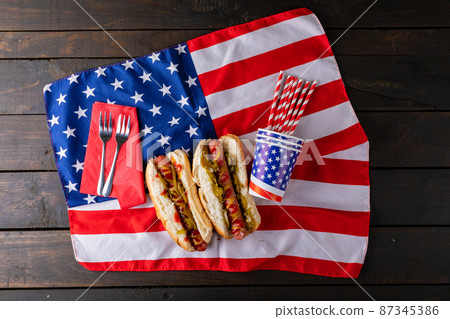 Hot dogs with jalapenos served on american flag with fork, straw and disposable cups at table 87345386