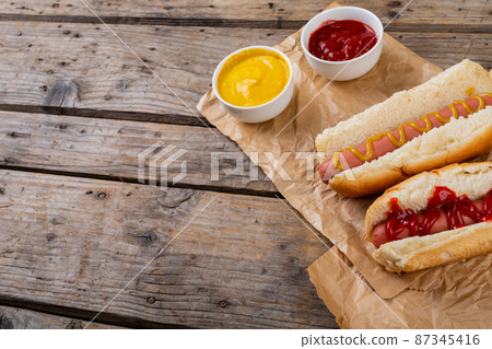 High angle view of hot dogs with tomato and mustered sauces on paper bags at table 87345416