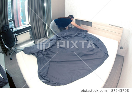 An Asian female maid making bed in hotel room. Housekeeper Making Bed. An Asian female maid making bed in hotel room. Housekeeper Making Bed. 87345798