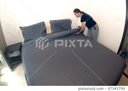 An Asian female maid making bed in hotel room. Housekeeper Making Bed. An Asian female maid making bed in hotel room. Housekeeper Making Bed. 87345799