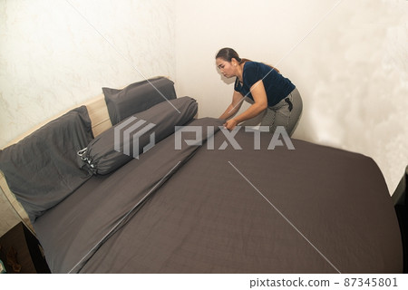 An Asian female maid making bed in hotel room. Housekeeper Making Bed. An Asian female maid making bed in hotel room. Housekeeper Making Bed. 87345801