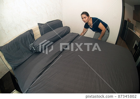 An Asian female maid making bed in hotel room. Housekeeper Making Bed. An Asian female maid making bed in hotel room. Housekeeper Making Bed. 87345802
