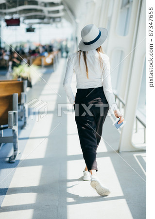 Young woman near window in an airport lounge waiting for flight aircraft. woman at the airport stands with tickets, overall plan. Young woman near window in an airport lounge waiting for flight aircraft. woman at the airport stands with tickets, overall plan. 87347658