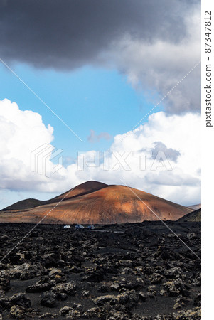 Amazing panoramic landscape of volcano craters in Timanfaya national park. Popular touristic attraction in Lanzarote island, Canary islans, Spain. Artistic picture. Beauty world. Travel concept. Amazing panoramic landscape of volcano craters in Timanfaya national park. Popular touristic attraction in Lanzarote island, Canary islans, Spain. Artistic picture. Beauty world. Travel concept. 87347812