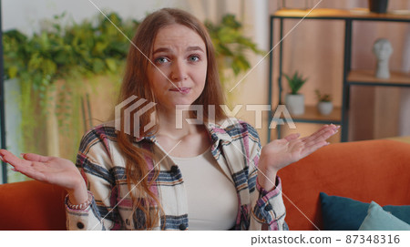 Pretty girl alone at home having doubts, no idea, being clueless and uncertain shrugs shoulders Pretty girl alone at home having doubts, no idea, being clueless and uncertain shrugs shoulders 87348316