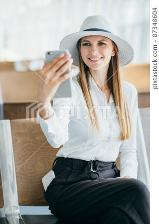 Woman talking on the phone at the airport terminal. Portarit of a young female traveler with a luggage and coffee cup and phone at the public transport stop on a sunny summer day Woman talking on the phone at the airport terminal. Portarit of a young female traveler with a luggage and coffee cup and phone at the public transport stop on a sunny summer day 87348604