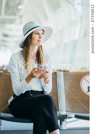 Woman Reading Phone Messages in Airport Waiting Room. Happy girl buying e-ticket, making hotel reservations and checking in online. Woman Reading Phone Messages in Airport Waiting Room. Happy girl buying e-ticket, making hotel reservations and checking in online. 87348612