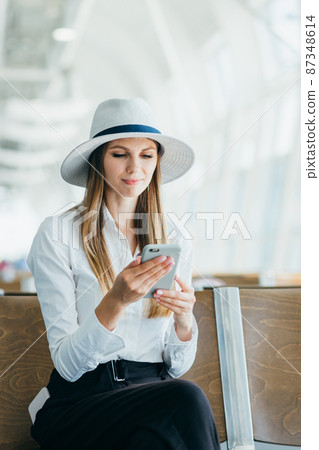 Casual young woman using her cell phone while waiting to board a plane at the departure gate 87348614