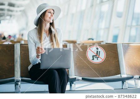 Young woman in international airport working on laptop while waiting for her flight. Young woman in international airport working on laptop while waiting for her flight. 87348622