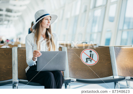 Business lady sitting at the airport on the background of a large window with a laptop on her lap, finishes work and approaches the window. Freelancer, The concept of work remotely from the office Business lady sitting at the airport on the background of a large window with a laptop on her lap, finishes work and approaches the window. Freelancer, The concept of work remotely from the office 87348623
