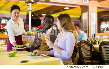 Polite Asian waitress serving dishes to biracial couple in restaurant 87349066
