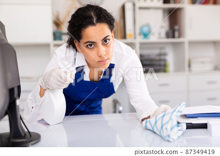 Female worker cleaning desk in office Female worker cleaning desk in office 87349419