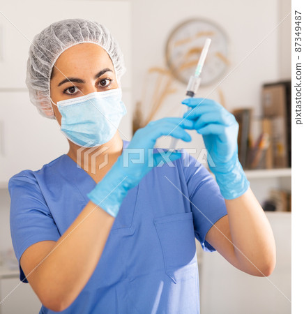 Girl nurse in mask holding syringe for injection Girl nurse in mask holding syringe for injection 87349487