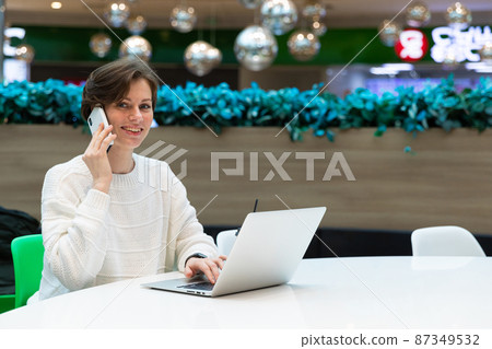 A photo of a young smiling happy woman who sits at the food court of a shopping center at a table 87349532