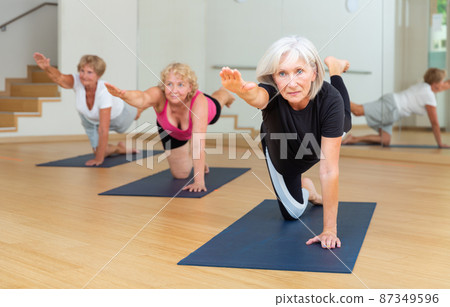 Mature woman practicing Dandayamna Bharmanasana during group yoga workout Mature woman practicing Dandayamna Bharmanasana during group yoga workout 87349596