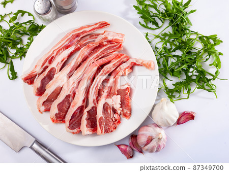 Raw hogget chops on plate with arugula, garlic and seasonings Raw hogget chops on plate with arugula, garlic and seasonings 87349700