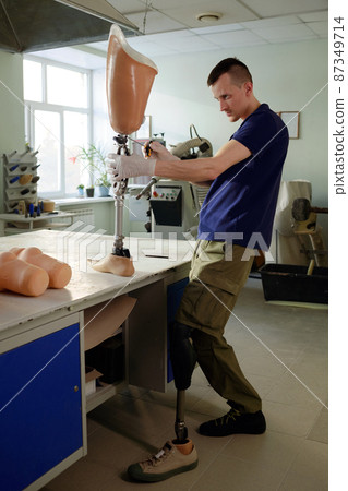 Manual worker with disability standing by table while fixing parts of mechanism Manual worker with disability standing by table while fixing parts of mechanism 87349714