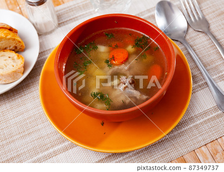 Soup in pork broth with potatoes, carrots, onions and herbs 87349737