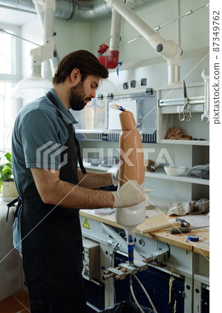 Side view of young specialist of manufactory creating new artificial limb Side view of young specialist of manufactory creating new artificial limb 87349762