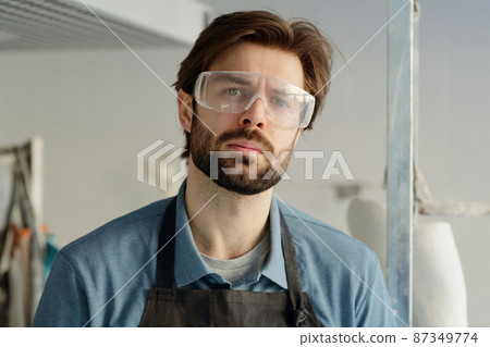 Young serious workman in apron and protective eyewear Young serious workman in apron and protective eyewear 87349774