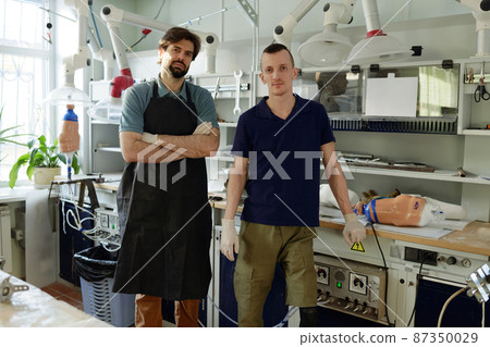 Two young specialists in workwear standing in large workshop Two young specialists in workwear standing in large workshop 87350029