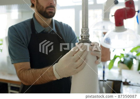 Gloved young male worker fixing thermoplastic sheet over prosthetic socket Gloved young male worker fixing thermoplastic sheet over prosthetic socket 87350087