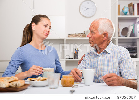 Senior man and young daughter sitting together with cup of tea Senior man and young daughter sitting together with cup of tea 87350097
