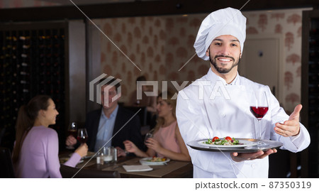 Positive chef with serving tray meeting guests 87350319